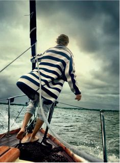 a man in striped shirt riding on the back of a boat under cloudy skies and water