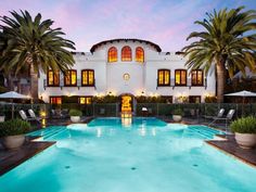 an outdoor swimming pool with lounge chairs and palm trees in front of a large white building