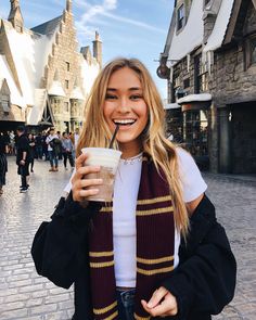 a woman holding a drink in her right hand and wearing a scarf around her neck