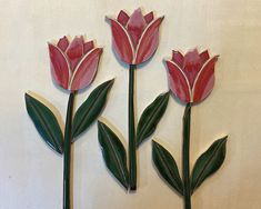 three red flowers with green leaves on a white wall