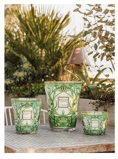 three green candles sitting on top of a wooden table next to some plants and trees