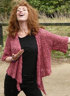 a woman with red hair wearing black pants and a pink crocheted cardigan