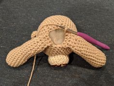 a crocheted stuffed animal is laying on the floor next to a knitting needle