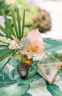 an arrangement of flowers and plants on a tropical table cloth with gold geometric vases