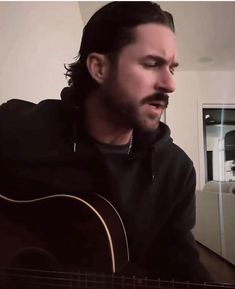 a man is playing an acoustic guitar in the living room with his eyes closed and mouth wide open