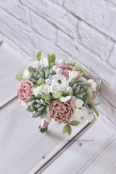 a bridal bouquet with pink, white and green flowers on a wooden table next to a brick wall