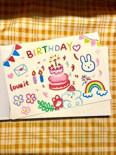 a birthday card with an image of a cake and rainbows on the front, sitting on a checkered tablecloth