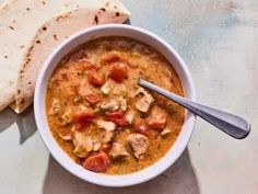 a bowl of chicken and tomato soup with pita bread