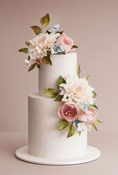 a three tiered white cake with flowers on it's side and leaves on the top