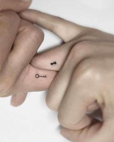 two hands holding each other with small tattoos on their thumbnails and one has an arrow in the middle