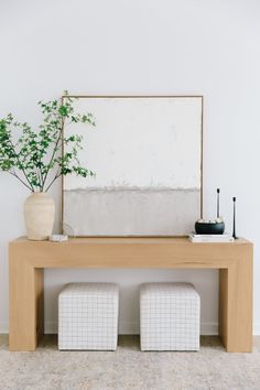 a wooden table with two stools and a plant on it in front of a mirror