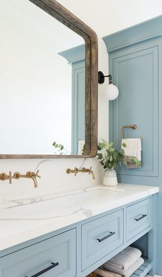 a bathroom with blue cabinets and white counter tops in front of a large mirror above the sink