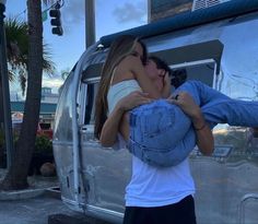 two people kissing each other in front of a silver truck with palm trees behind them