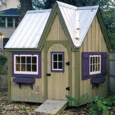 a small wooden house with purple shutters on the windows and a white roof sits in front of a fence