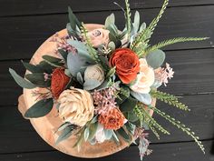 an arrangement of flowers in a wooden bowl on a black table with wood planks