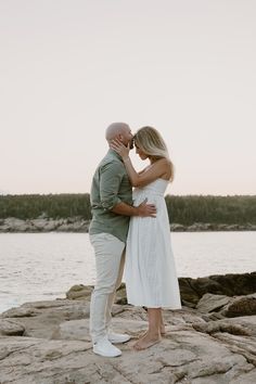 an engaged couple kissing on the rocks by the water