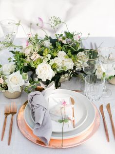 the table is set with white and pink flowers, silverware, and napkins