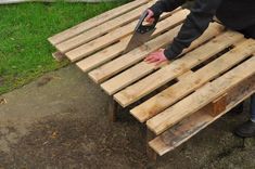 a person with a pair of scissors on top of a wooden pallet bench in the grass