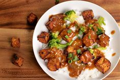 a white plate topped with meat and broccoli covered in gravy on top of rice