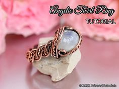 an image of a ring made with wire and stone on top of a rock next to pink flowers