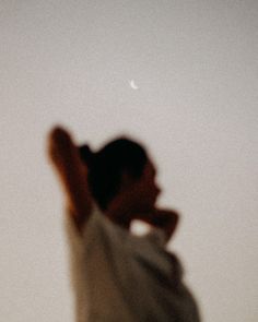 a blurry image of a person holding a cell phone up in the air with a half moon behind them