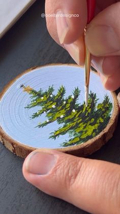 a person is using a needle to paint a piece of wood with trees on it