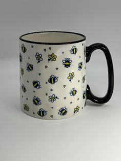 a black and white coffee mug with yellow bees on it's side, in front of a gray background