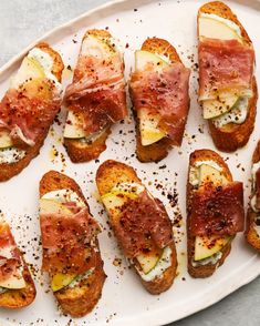 several pieces of bread with meat and cheese on them sitting on a white platter