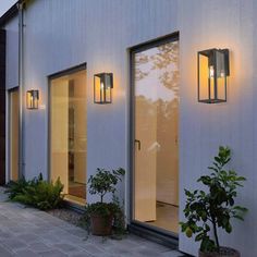 the outside of a house with three lights on and plants in pots next to it