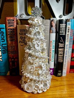 a white christmas tree made out of buttons on a wooden table next to some books