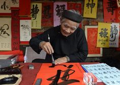 an old man is doing something in front of him at a table with chinese calligraphy on it