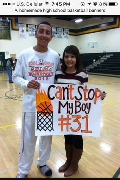 two people standing on a basketball court holding a sign that says can't stop my boy