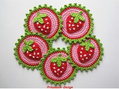 four crocheted strawberry coasters with green and pink trimming on white surface