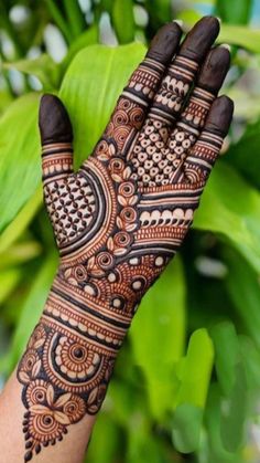 a hand with henna on it and some green leaves in the backgroud