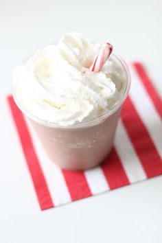 a cup with whipped cream and a candy cane in it on a red and white striped napkin