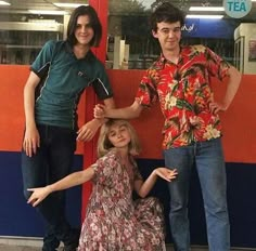 three people standing next to each other in front of a red and blue train station