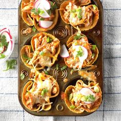 an overhead view of some taco shells with toppings on a baking sheet next to a glass of water