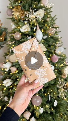 someone holding up a christmas present in front of a tree