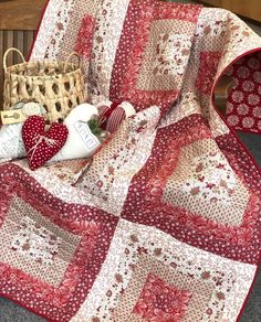 a red and white quilt sitting on top of a wooden bench next to a basket