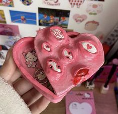 a pink heart shaped object held in someone's hand with pictures on the wall behind it