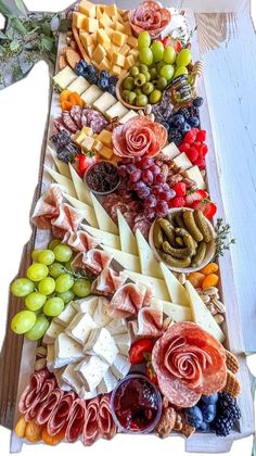 an assortment of cheeses, meats and vegetables on a platter with grapes