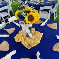 a vase with sunflowers is sitting on a blue table cloth at an outdoor event