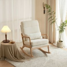 a white rocking chair sitting on top of a rug next to a table with a lamp