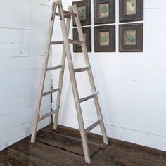 an old wooden ladder leaning against a wall with four framed pictures on the wall behind it