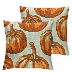 two pillows with pumpkins on them sitting next to each other in front of a white background