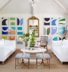 a living room filled with white furniture and paintings on the wall above it's coffee table