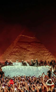 a crowd of people taking pictures with their cell phones in front of an egyptian pyramid