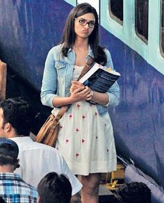 a woman standing in front of a train holding a book