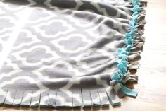 a gray and white blanket with blue tassels on the edge sitting on a wooden floor