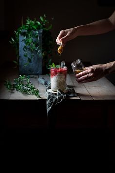 someone is adding ingredients to a blender on a wooden table with plants in the background